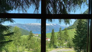 Paesaggio montuoso con un lago, vegetazione e alcuni edifici, vista da una finestra.