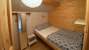 Una camera da letto piccola e accogliente con soffitto e pareti in legno, un letto singolo con copripiumino floreale e un piccolo sgabello.