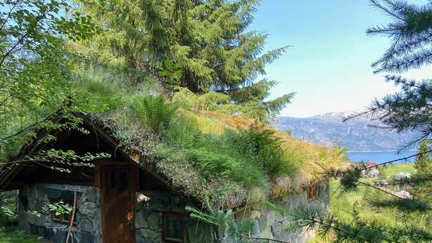 Una baita rustica con facciata in pietra e porta in legno, immersa nel verde e con vista su un lago.