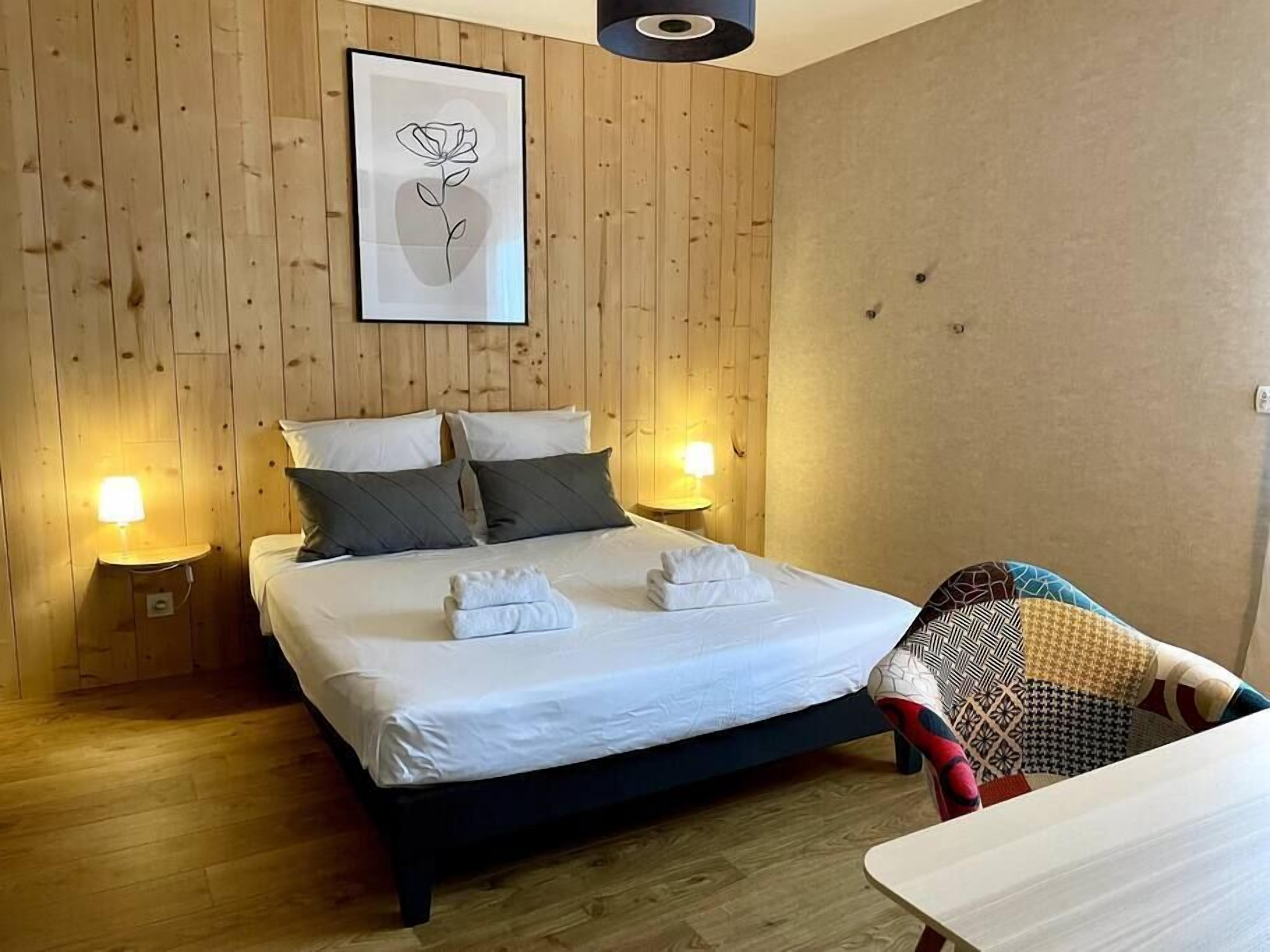 Una cama bien hecha con sábanas blancas y dos almohadas, una obra de arte enmarcada de una rosa en la pared, y dos lámparas de noche.