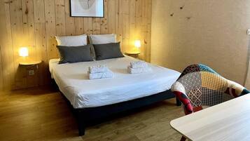 Una cama bien hecha con sábanas blancas y dos almohadas, una obra de arte enmarcada de una rosa en la pared, y dos lámparas de noche.