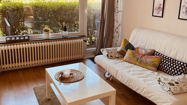 Uma sala de estar moderna com um sofá branco, uma mesa de centro branca e uma janela ampla com vista para uma área residencial.