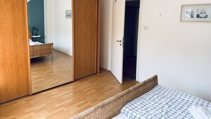 Quarto com guarda-roupa de madeira, cama com colcha estampada e porta que dá para outro cômodo.