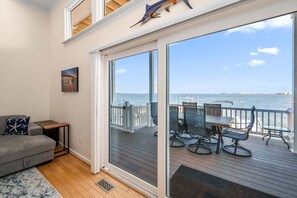 Un balcone con vista sul mare, un'area pranzo con sedie e tavolo, un divano grigio e un quadro appeso al muro.