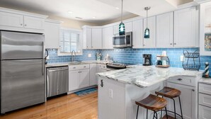 A modern kitchen with white cabinets, a stainless steel refrigerator, a marble island, and bar stools.
