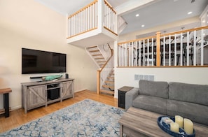 A spacious living room with a staircase, a flat-screen TV, a grey sofa, and a wooden coffee table.