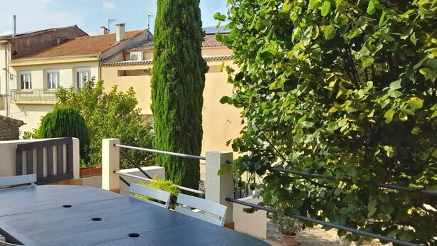 A rooftop terrace with a table and chairs, surrounded by greenery and buildings in the background. - La Vigneronne de Mamie (Puimisson)