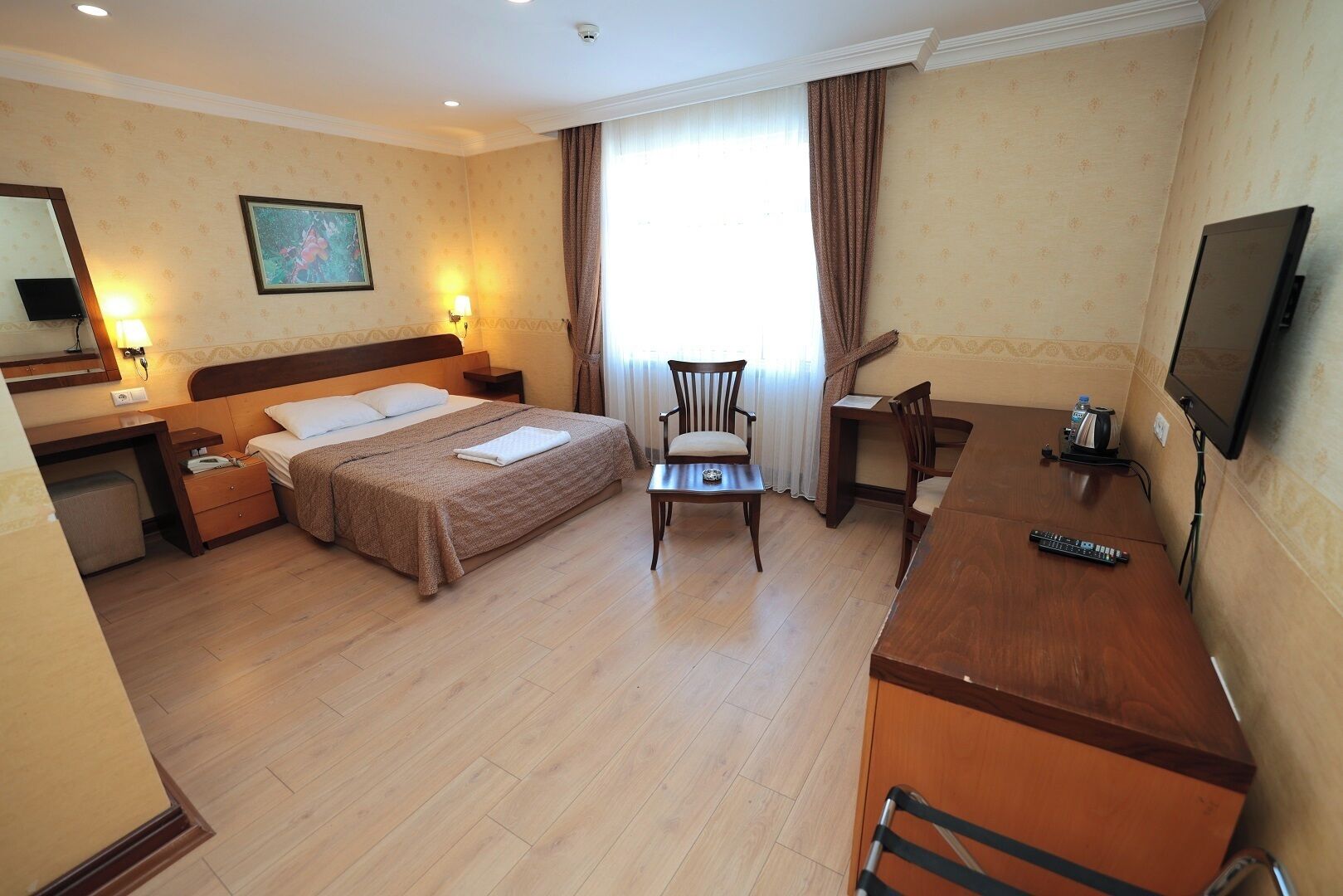 A hotel room with a bed, a desk, a chair, a television, and a window with curtains.
