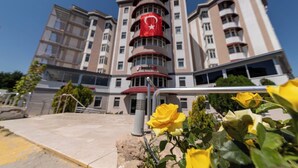 Un hotel de varios pisos con una llamativa bandera roja en la fachada, balcones y un cielo despejado.