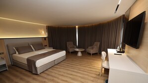 Habitación de hotel con cama, dos sillones, escritorio, televisor y una mesita.