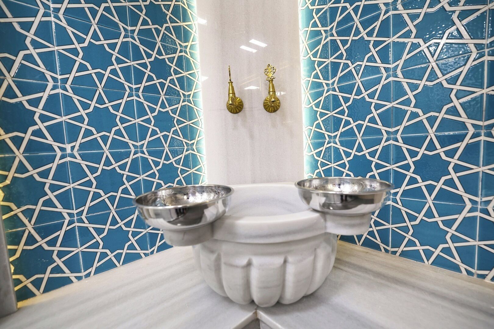 A bathroom with a geometric tile pattern, a white pedestal, and two metal bowls.