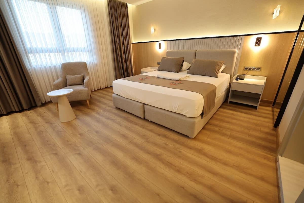 Moderni hotellihuone, jossa on suuri sänky, yöpöydät, pieni pyöreä pöytä ja tuoli.
