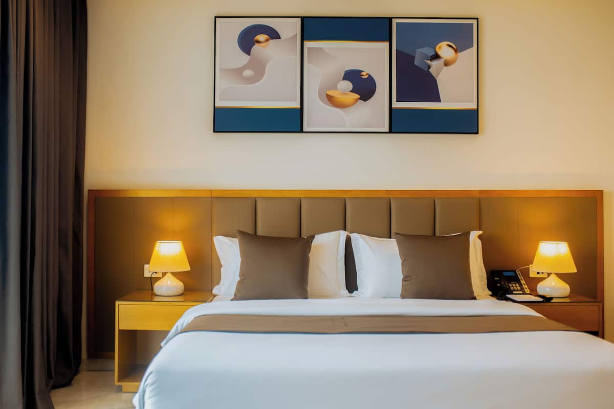 A hotel room with a large bed, two bedside tables with lamps, a telephone, and three abstract paintings on the wall.