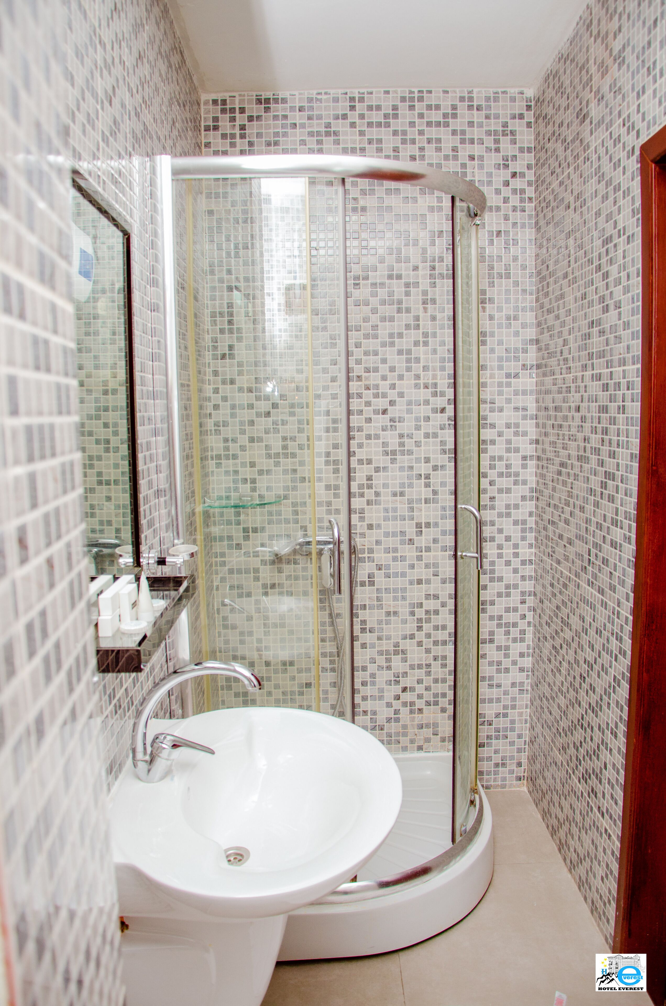 Un baño con ducha envuelta en vidrio, un lavamanos y un espejo.