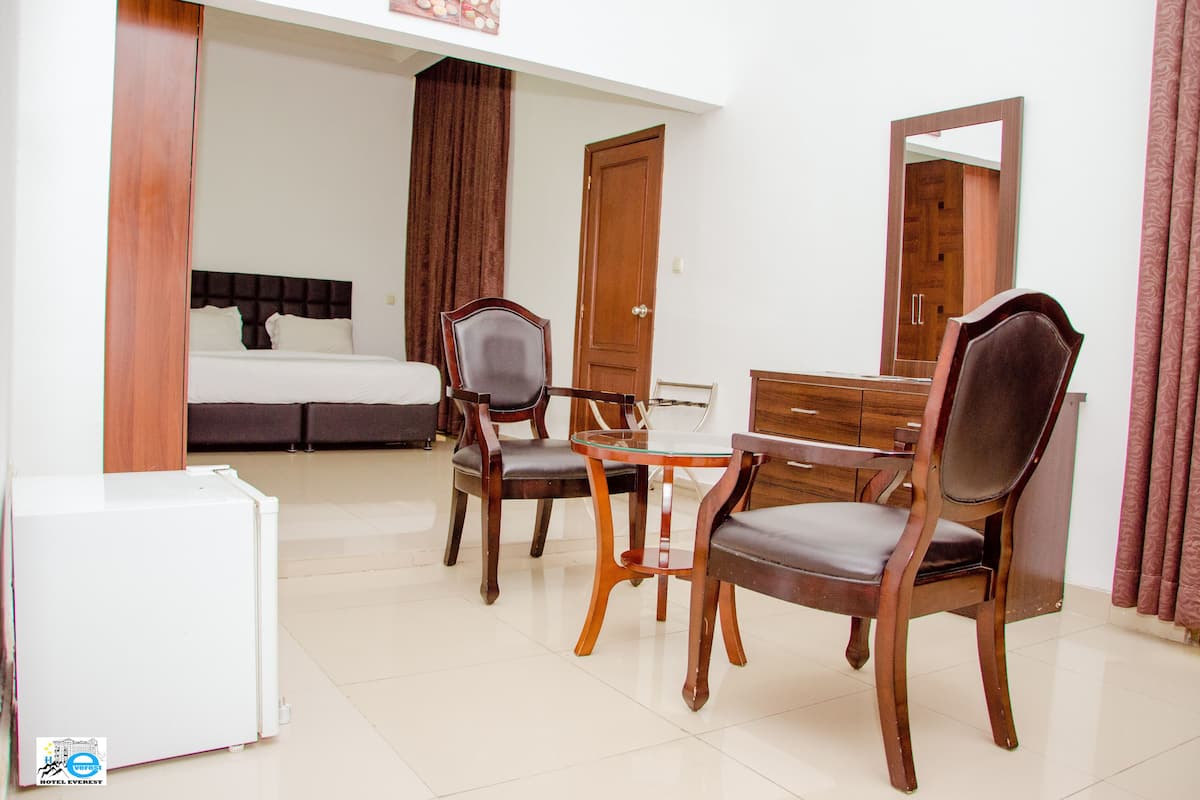 A hotel room with a bed, two wooden chairs, a small table, a dresser, and a mirror.