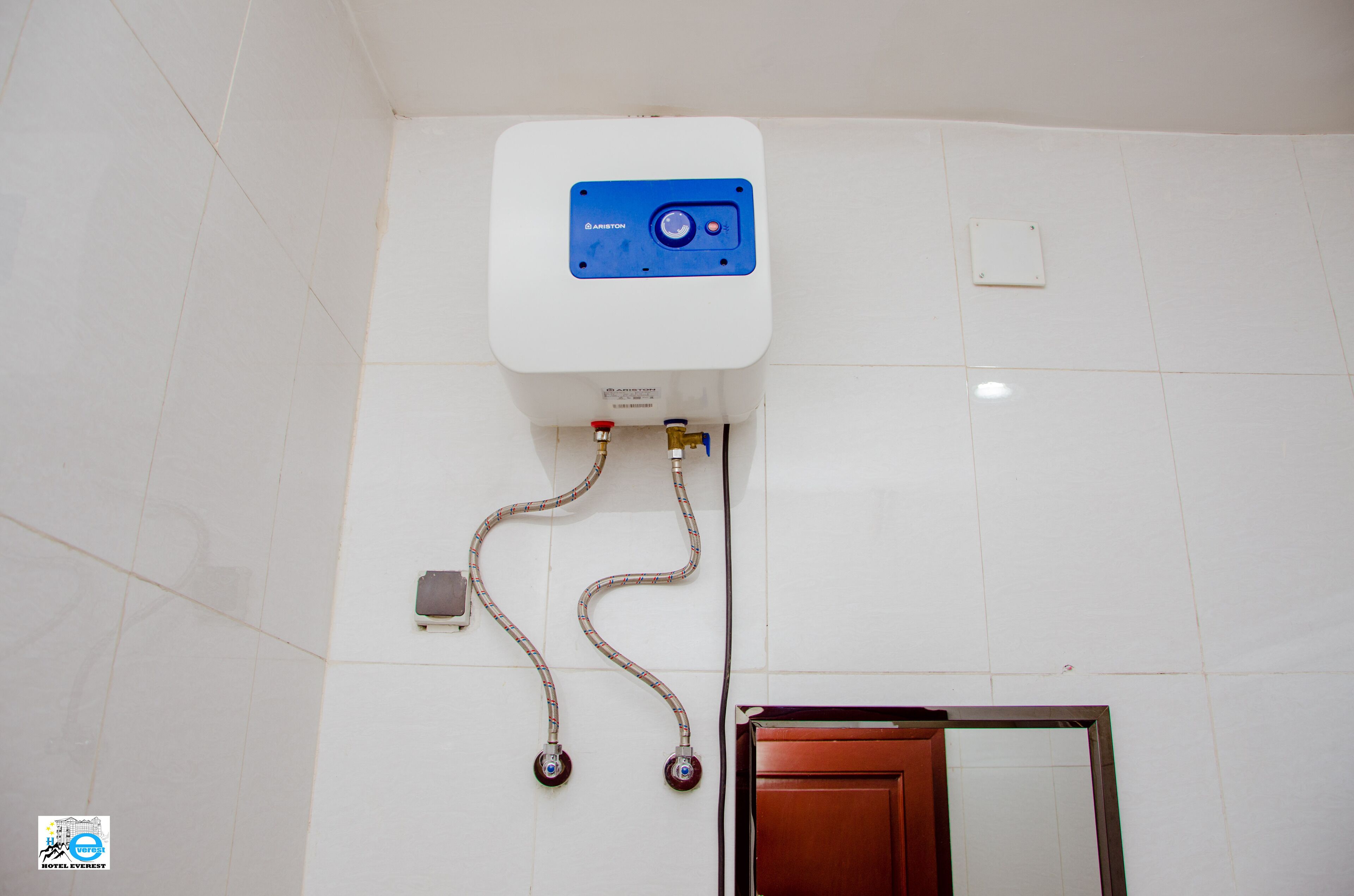 Een witte betegelde muur met een witte boiler boven een deur.