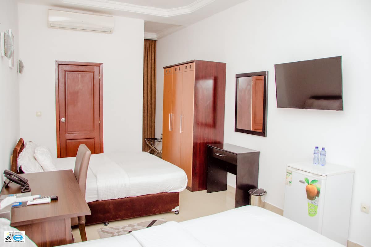 A hotel room with a bed, a desk, a wardrobe, a television, and a refrigerator.