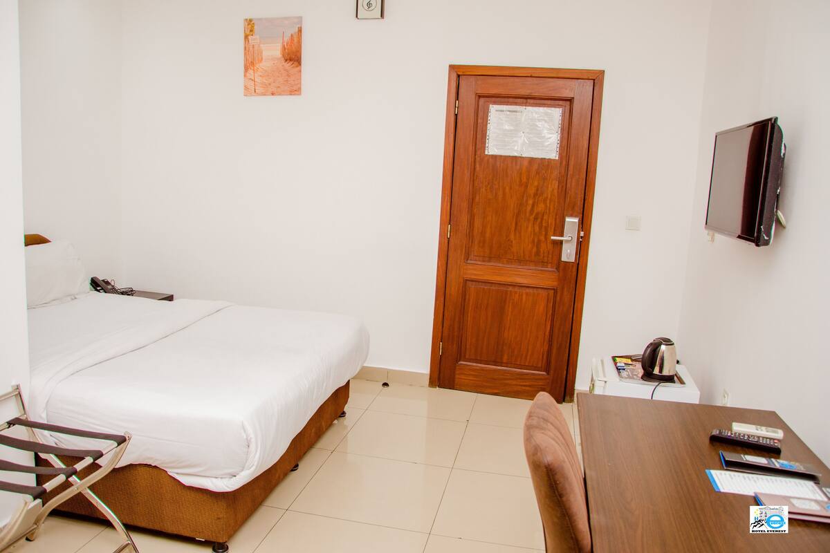 A hotel room with a bed, a desk with a computer, a chair, a TV, and a door.
