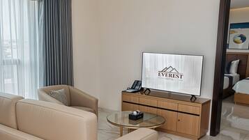 A hotel room with a sofa, a glass coffee table, a television, and a wooden cabinet.