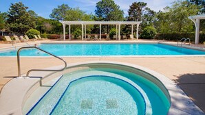 Une piscine avec un jacuzzi, des chaises longues et un espace salon couvert.
