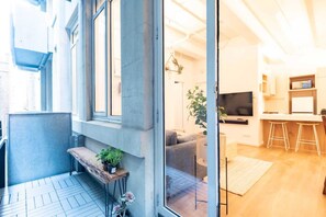 Un apartamento moderno con balcón, sala de estar con sofá y televisor, y cocina con taburetes.