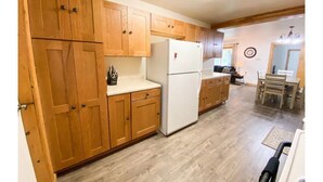Una cocina con armarios de madera, un refrigerador blanco y un comedor con una mesa y sillas.