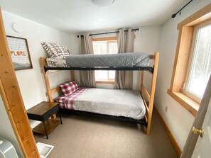 A bunk bed with a desk and chair, a window with curtains, and a framed picture on the wall.