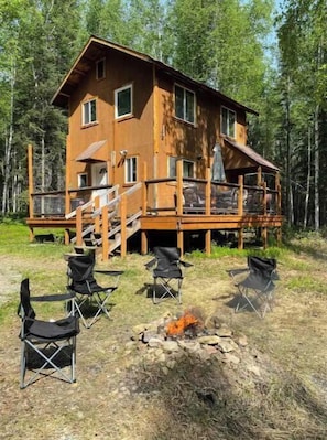 A wooden cabin with a deck, surrounded by trees.
