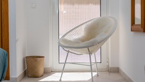Una sedia bianca con seduta e schienale intrecciati, posta di fronte a una porta in vetro, con una parete in pietra sullo sfondo.