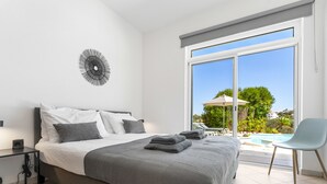 Camera da letto con un letto grande, un comodino, una sveglia a parete e vista su una piscina esterna.