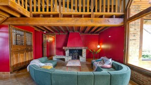 A cozy living room with a stone fireplace, wooden beams, and a curved green sofa.
