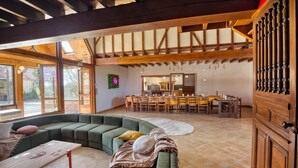 A spacious living area with a curved green sofa, a dining table with chairs, and a kitchen in the background.