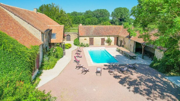 A courtyard with a swimming pool, lounge chairs, and stone buildings.