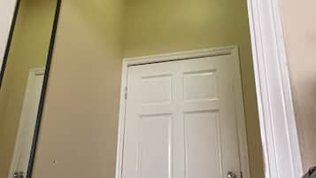Una puerta blanca con un espejo en la pared, una lámpara en el techo y una pared lisa.