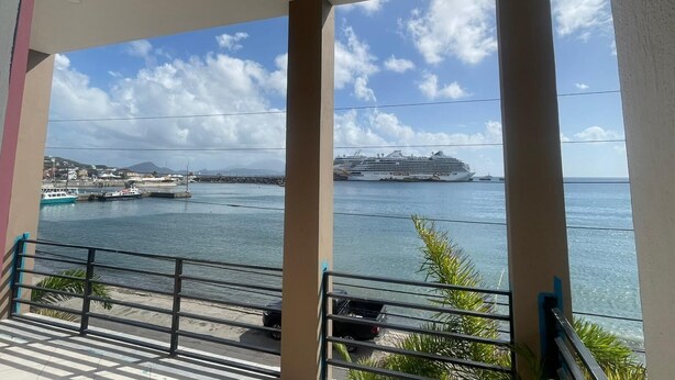 A balcony with a view of the sea, a cruise ship, and a distant shoreline with buildings. - The Colosseum (Basseterre)