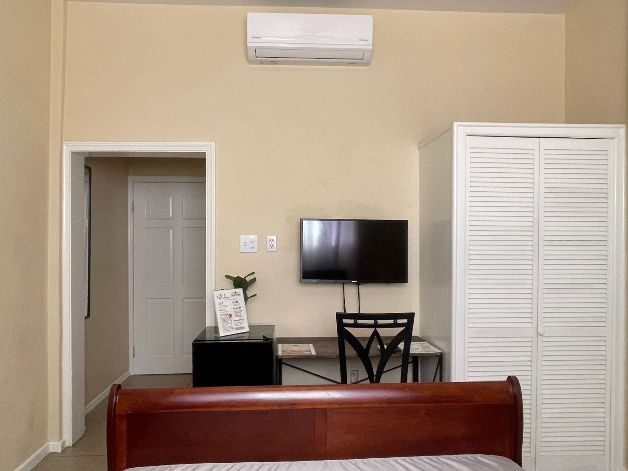 A hotel room with a bed, a desk with a chair, a television on the wall, and a white closet.