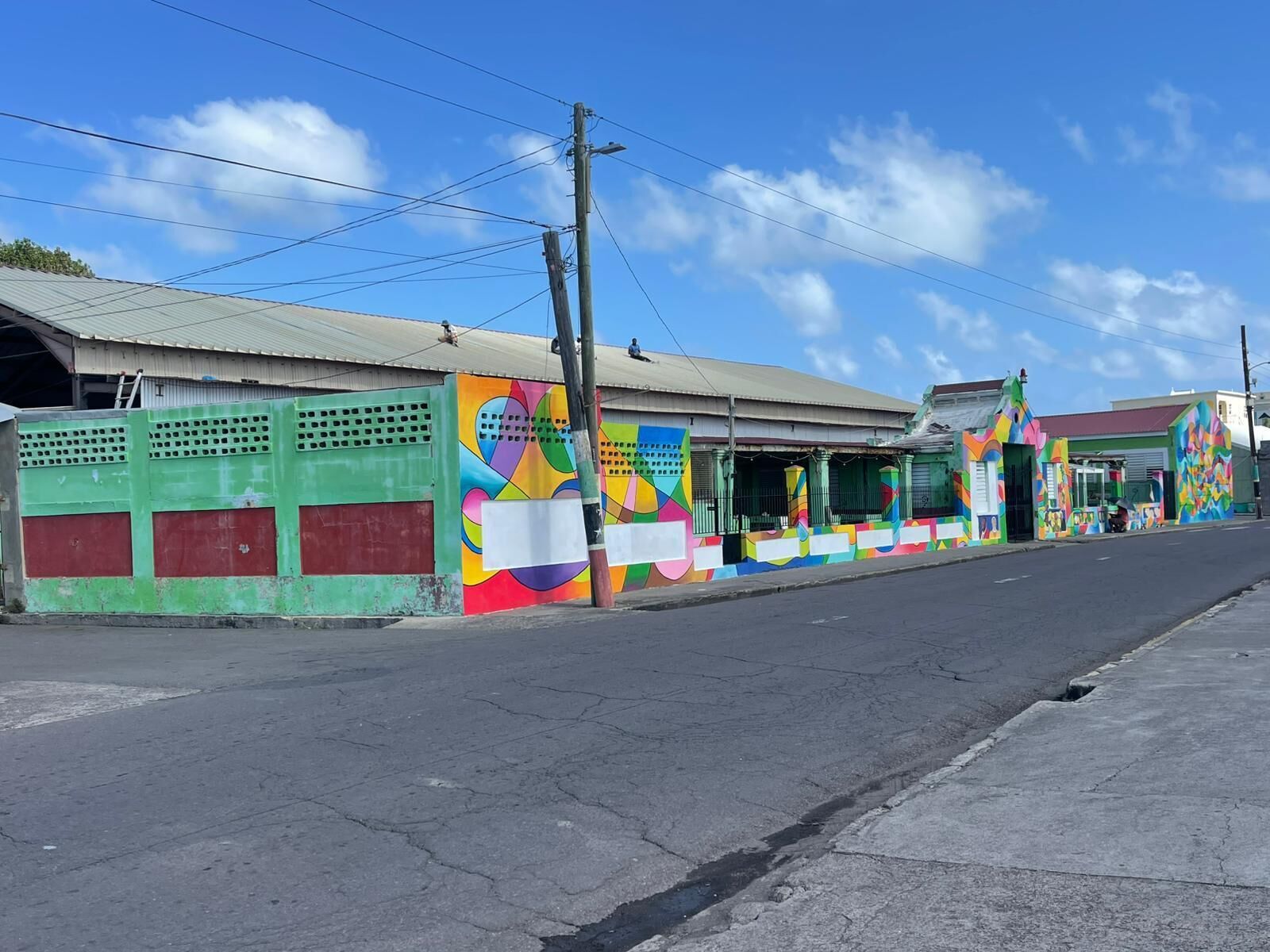 A street with colorful murals on buildings, a clear sky, and a road with visible cracks.