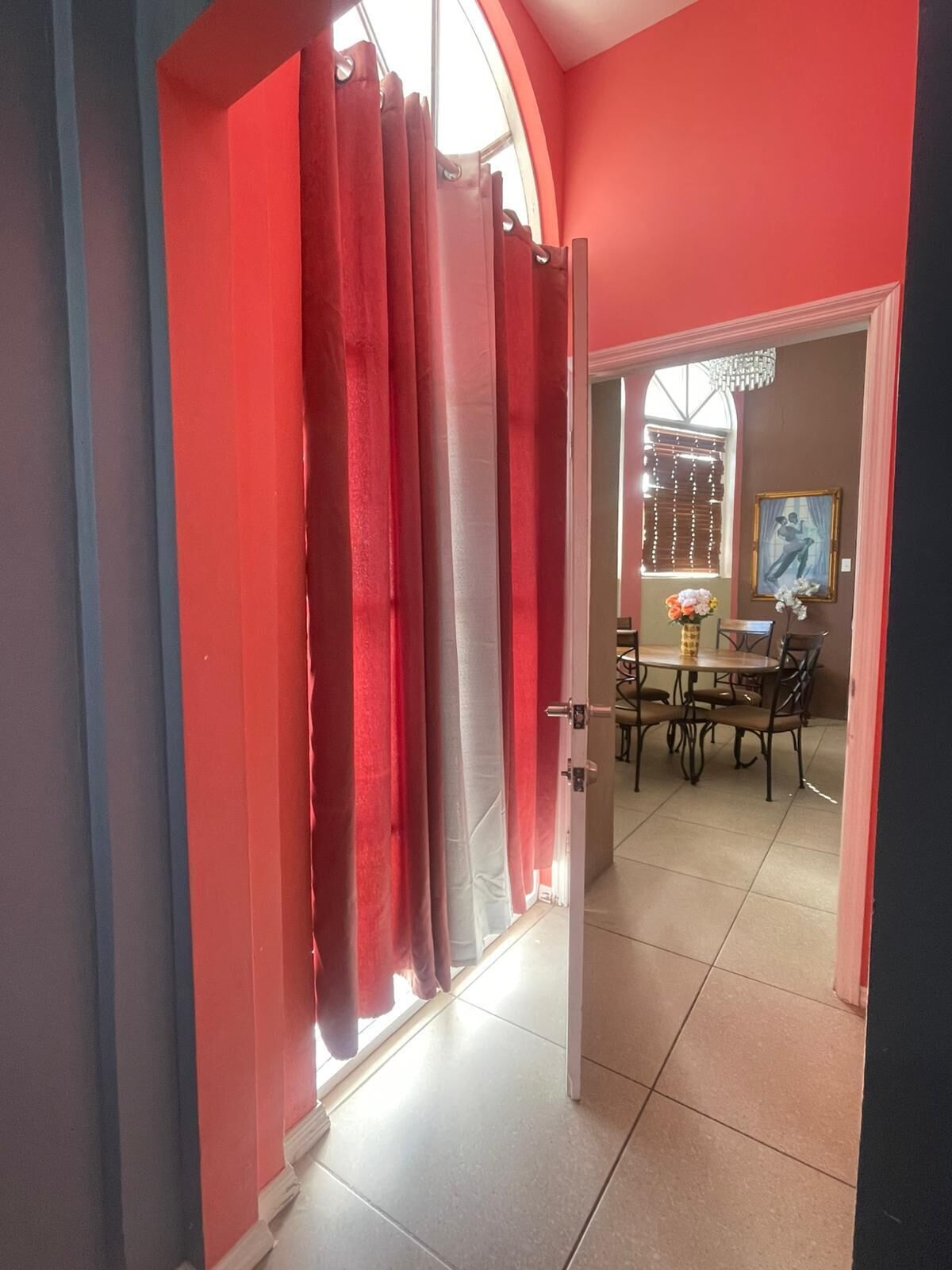 A room with a dining area, a table with chairs, and a window with curtains.