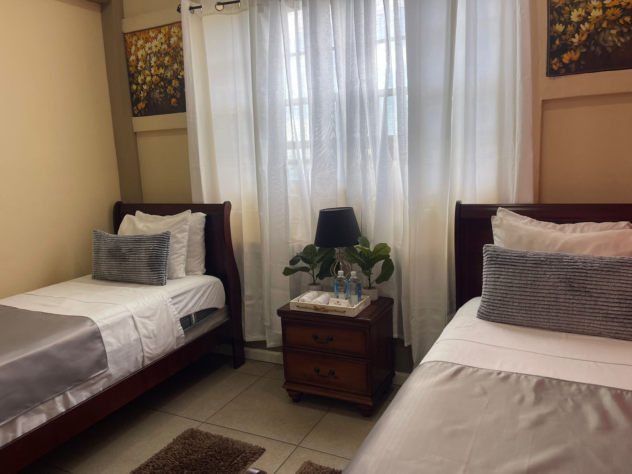 A hotel room with two beds, a nightstand, a lamp, and a potted plant.