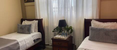 A hotel room with two beds, a nightstand, a lamp, and a potted plant.