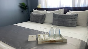 A hotel room with a neatly made bed, a tray with bottled water, a welcome card, and a potted plant. - The Colosseum (Basseterre)