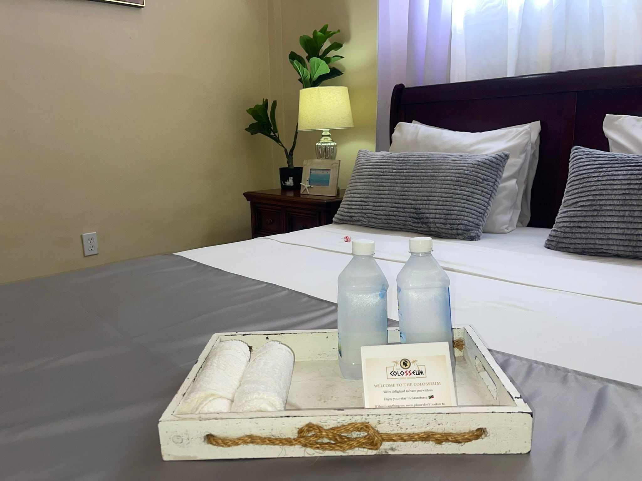 Een hotelkamer met een net opgemaakt bed, een nachtkastje met een lamp en een dienblad met toiletartikelen.