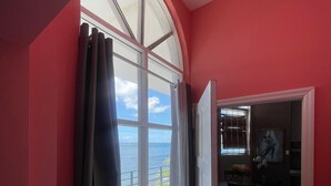 A room with a large arched window, a door leading to another room, and a view of the sea. - The Colosseum (Basseterre)