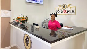 A reception desk with a monitor displaying a building, a logo for 'The Colossum Guest House', and a certificate on the wall. - The Colosseum (Basseterre)