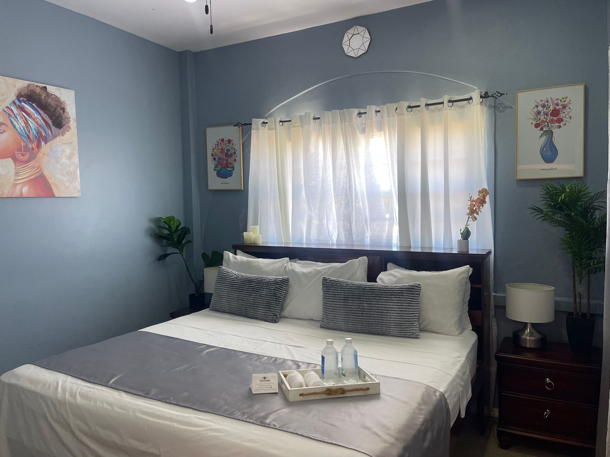 Un dormitorio con cama, mesitas de noche, un reloj y obras de arte en las paredes.