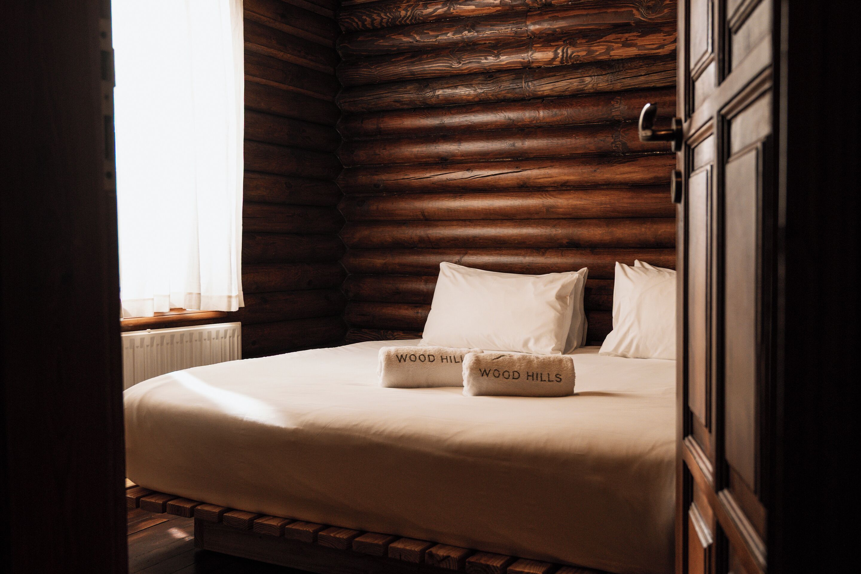 A wooden log cabin room with a bed, two pillows, and a window with curtains.