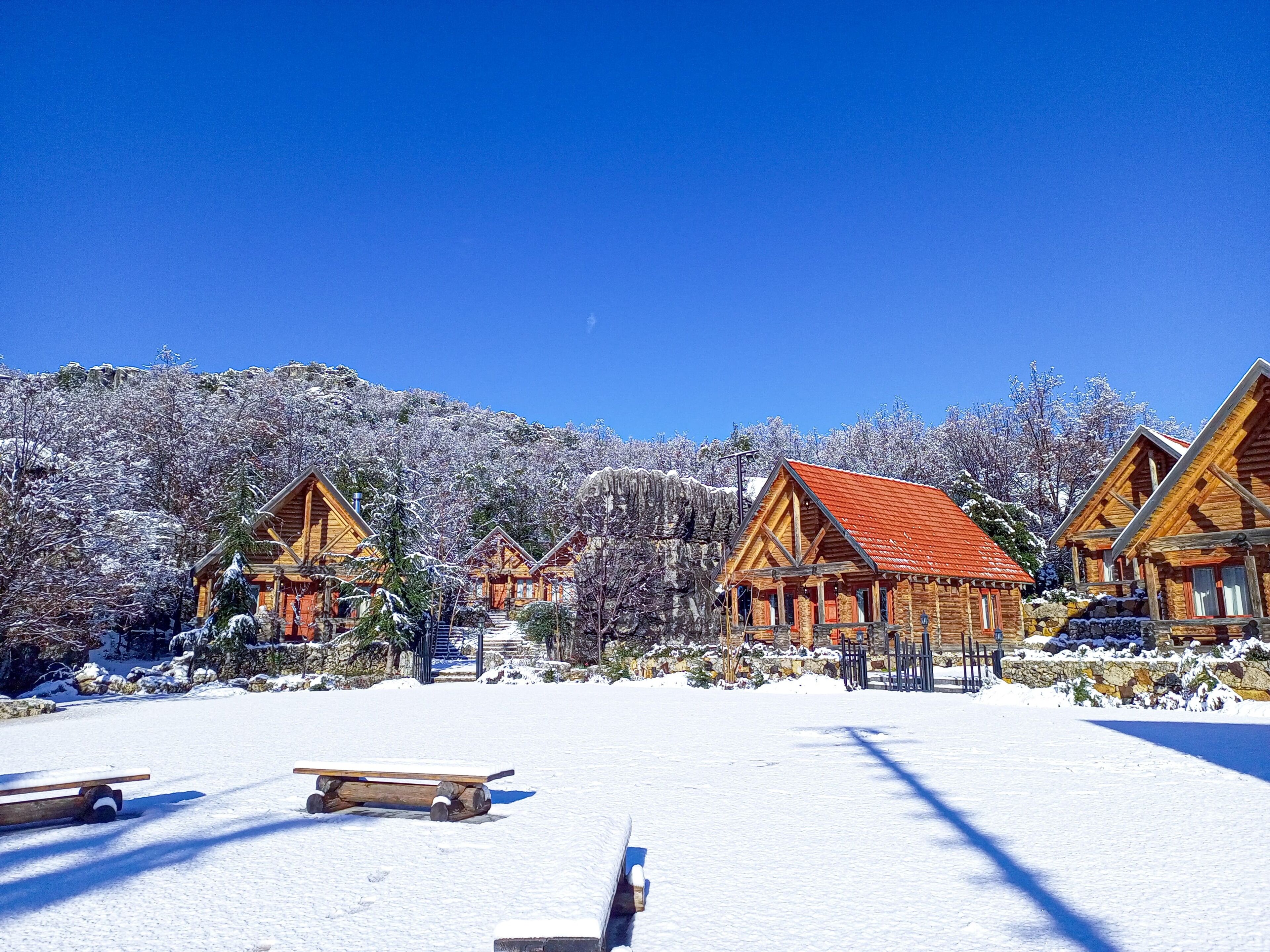 Una cabaña nevada con cabañas de madera y un cielo azul despejado.
