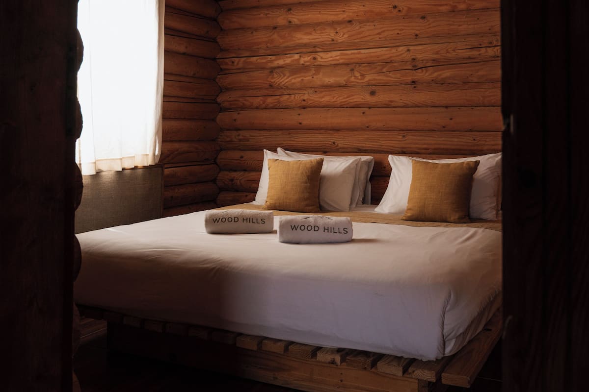A wooden cabin room with a bed, pillows, and a window.