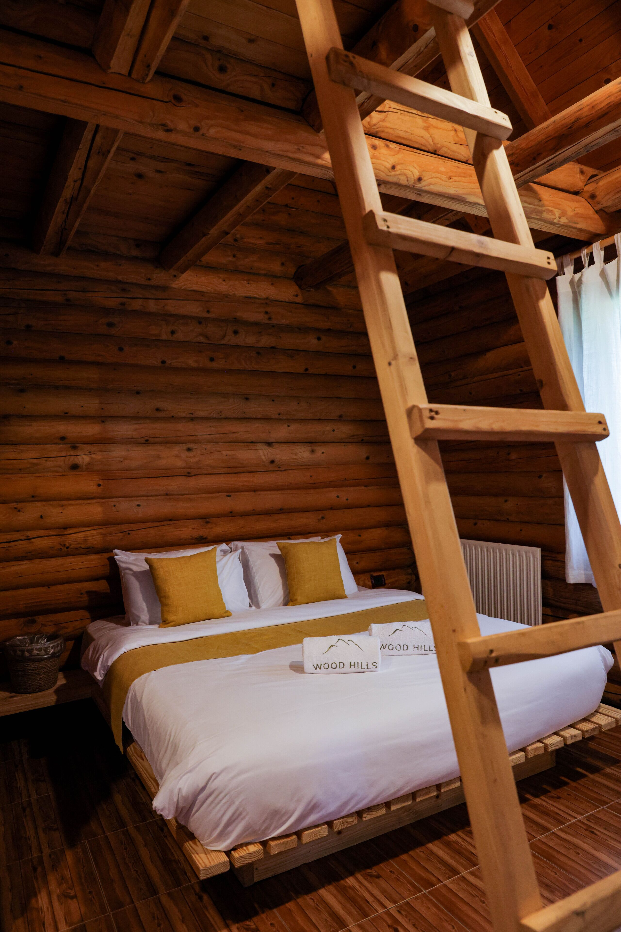 A wooden cabin room with a bed, a ladder, and a window.