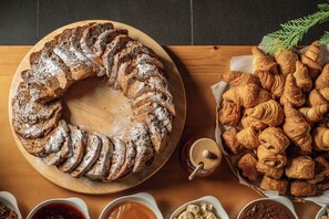 A wooden table with a braided bread, a basket of croissants, and small bowls of spreads. - Wood Hills Hotel & Resort (Mayrouba)